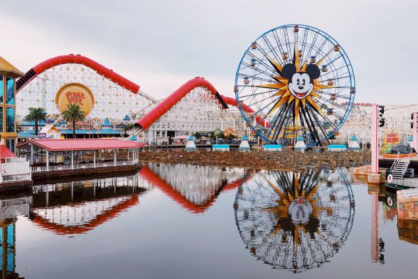 Amusement park with a large Ferris wheel and roller coaster, reflected in the water, featuring a familiar cartoon character’s face.