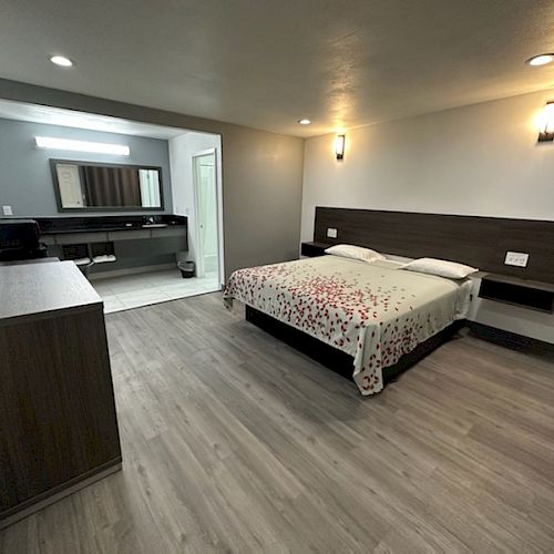 A modern hotel room with a bed, flat-screen TV, dresser, and an open bathroom vanity area.