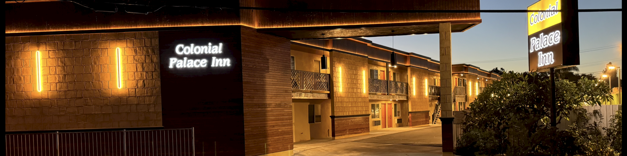 The image shows the exterior of a motel named Colonial Palace Inn, illuminated by lights with a driveway and signage visible at dusk.